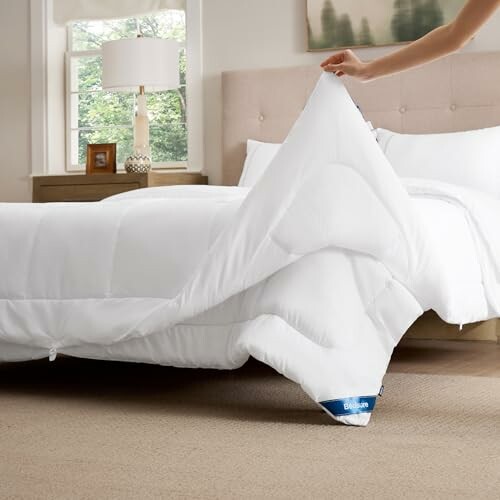 Hand richtet weiße Bettdecke auf Bett.